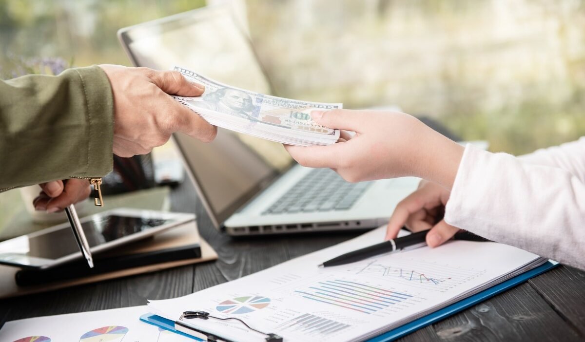 Business transaction showing cash being exchanged over financial documents with a laptop.