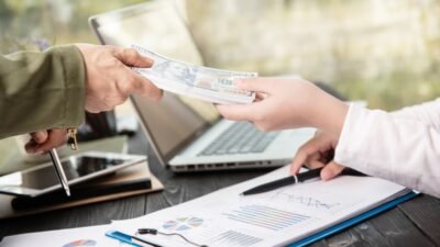 Business transaction showing cash being exchanged over financial documents with a laptop.